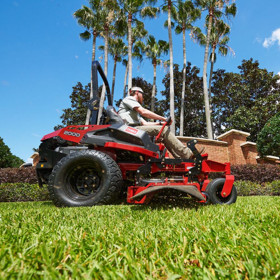 Man on a Z Master 2000 mower mowing lawn showing side discharge chute.