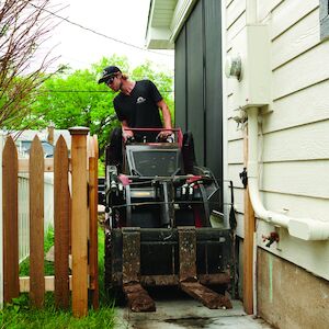 White male operating Dingo TX 1000 with forks attach going through a back yard gate.