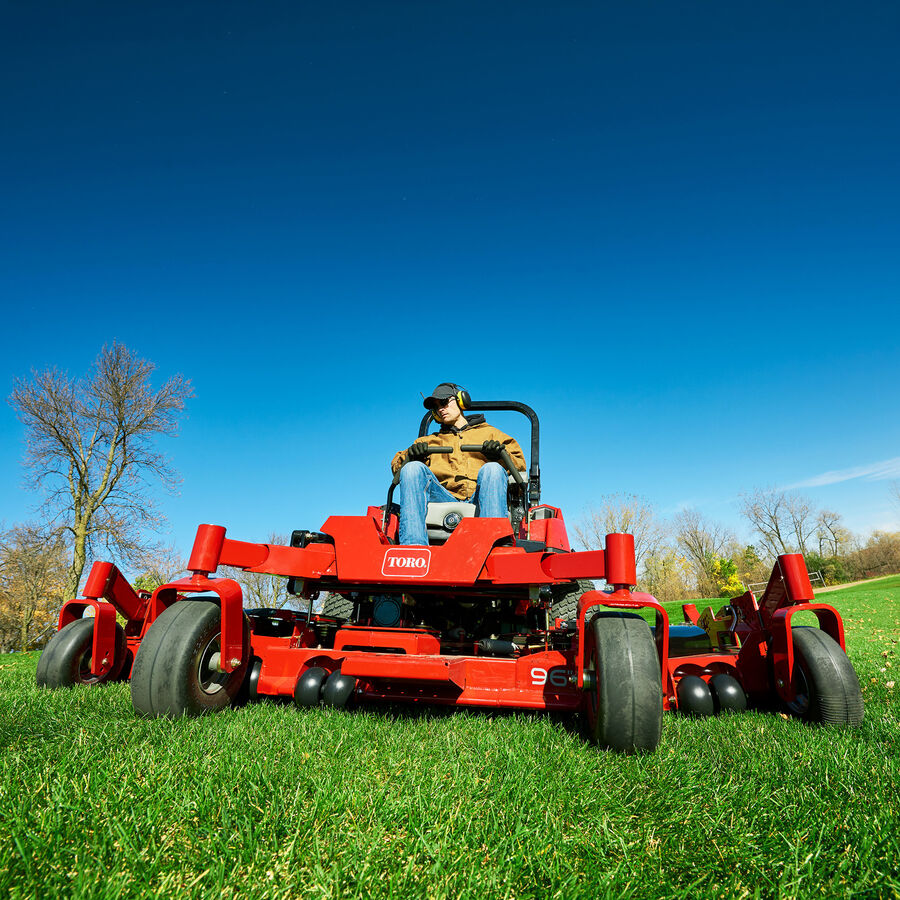 Man on a Toro Z Master 7500 series mower - mowing a park with a baseball field in the background.