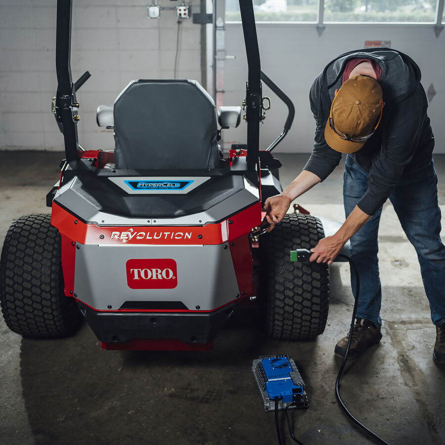 A man holding the plug in for Z Master Revolution mower - about to plug the mower in to charge it.