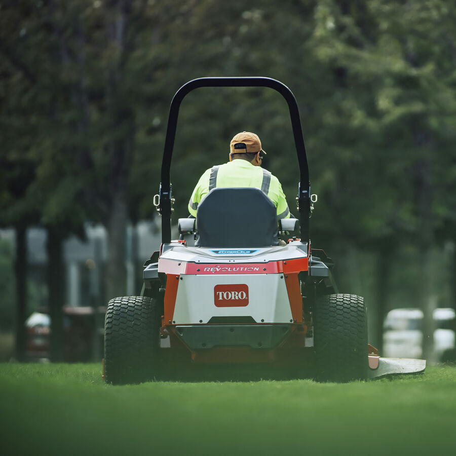 Man on a Toro Z Master Revolution series mower - mowing a lawn, image showing mower from the back.