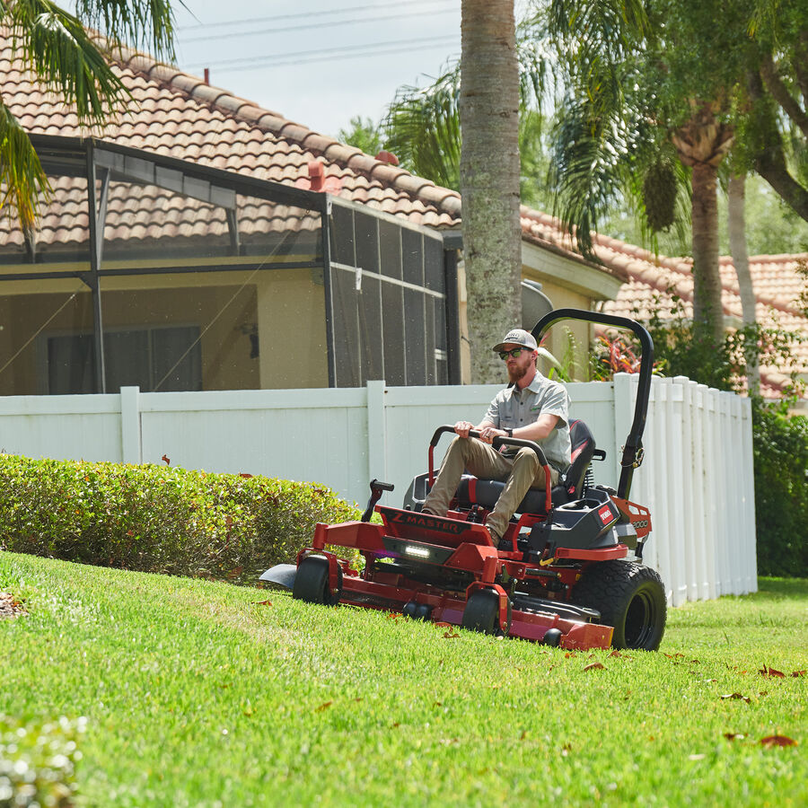 Z Master 2000 Series mower in use - man on mower mowing by a hedge with white fence behind it