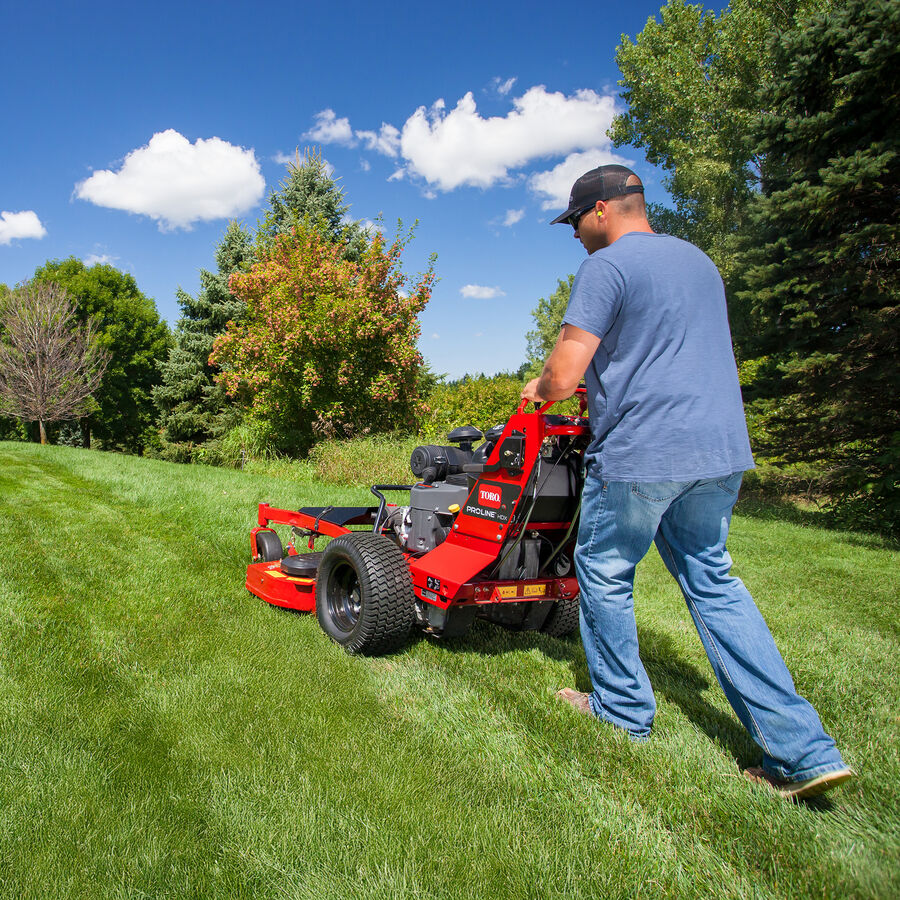 Man mowing with a Toro Proline Midsize mower mowing up a slight incline with pine trees to his right of the mower.