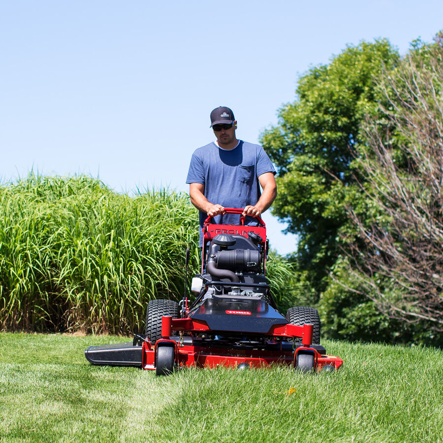 Man mowing with a Toro Proline Midsize mower mowing grass with trees in the background