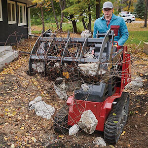 Male operating TX700 using the grapple rake picking up rocks and twigs