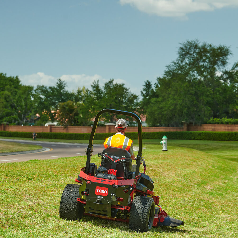 Man on a Z Master 2000 mower mowing lawn with a 2 lane road to the left side.