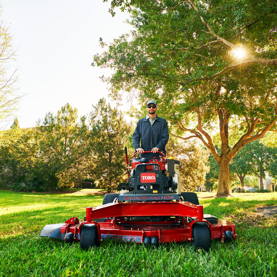 GrandStand® HDX Gas Stand-On Mower in use - mowing with tree in background