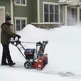 Man using snow blower on driveway by front walkway of a house