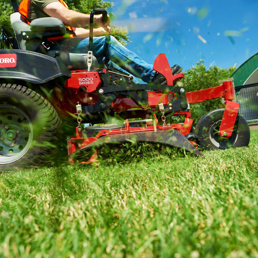 A close up of a Toro Z Master 5000 mower's side chute - grass is being mowed and discharged through the chute on to the grass.