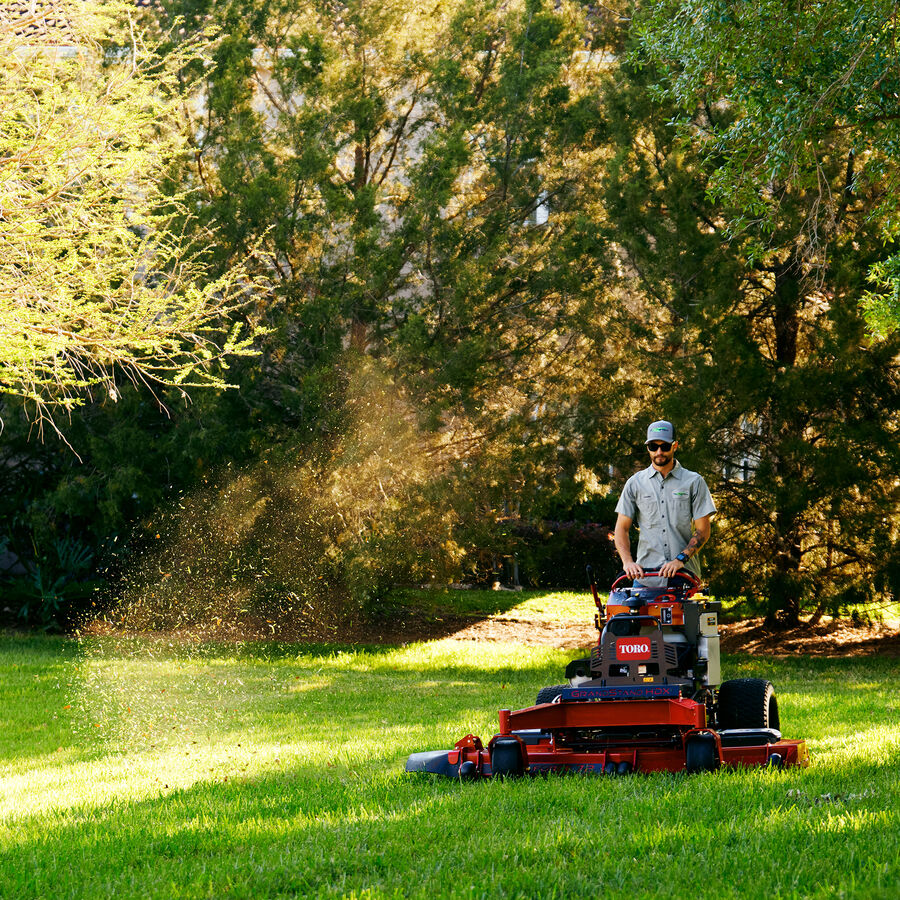 GrandStand® HDX Gas Stand-On Mower in use - mowing a park with trees in background
