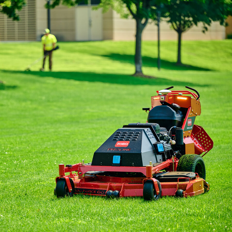 Toro Proline Autonomous Mower on grass with a landscape contractor using a trimmer in the background
