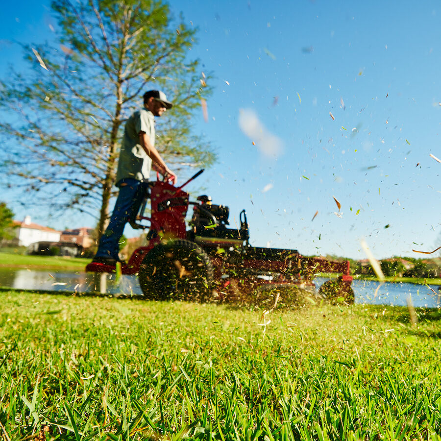 GrandStand® HDX Gas Stand-On Mower in use - mowing with trees and lake in background