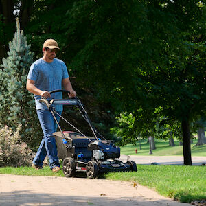 Man mowing grass along the side of a sidewalk