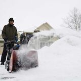 Man using snow blower on driveway in front of garage. 