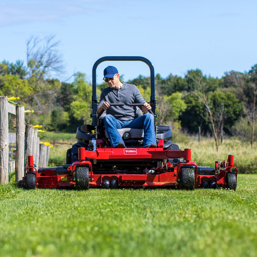 Man on a Toro Z Master 7500 series mower - mowing a grass next to a wooden fence with trees in the background.
