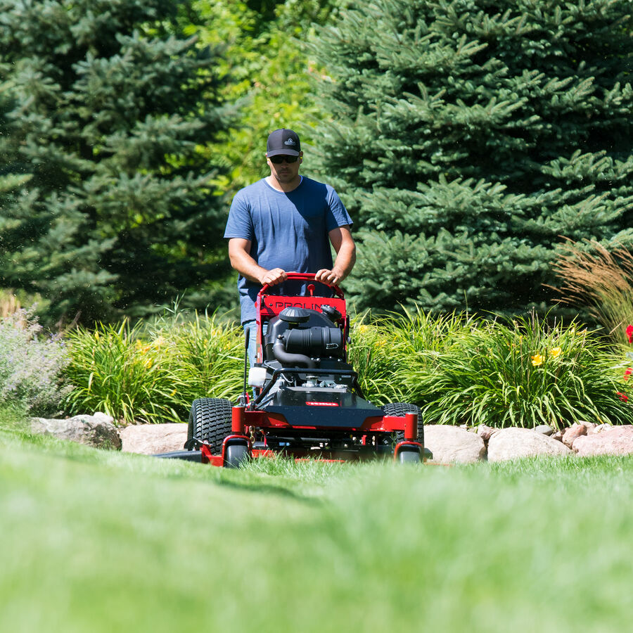 Man mowing with a Toro Proline Midsize mower mowing pine trees are in the background.