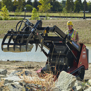 Dingo TX1300 dropping rock with a grapple rake.