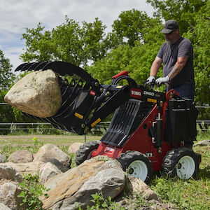Dingo 322 with the grapple rake carrying a rock.