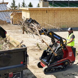 White male operating the Dingo TX 1000 with a bucket attach dumping sod.