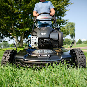 Close up image of the front end of the mower with a man behind it, pushing the handle to engage the mower