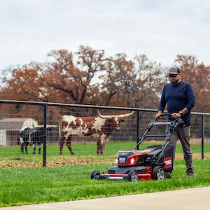 Grass Cut on a Single Charge - man mowing grass near sidewalk and cattle pen