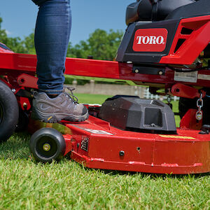 Image of person's leg standing on the deck on the zero turn mower
