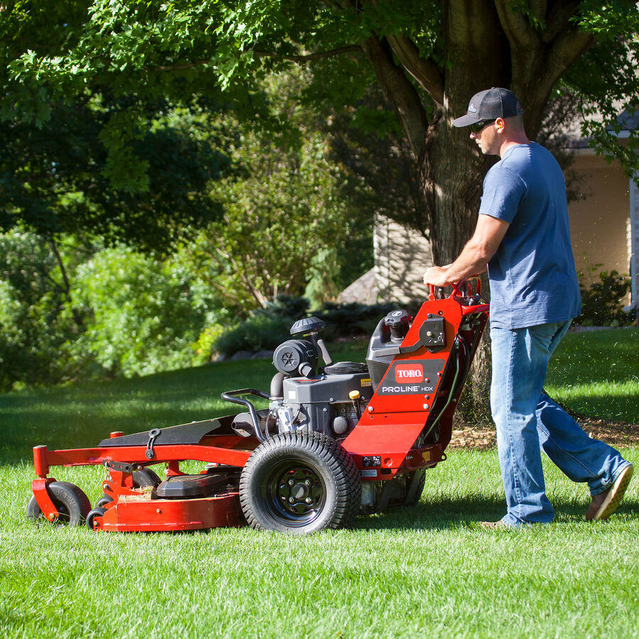 Man mowing with a Toro Proline Midsize mower mowing grass with trees in the background.