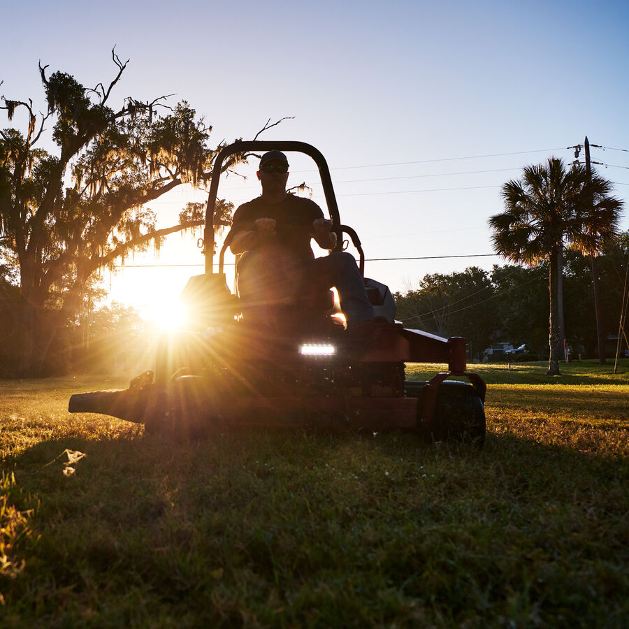 Man using a Z Master 2000 mower at dusk - sun is behind mower showing the headlight of the mower on.
