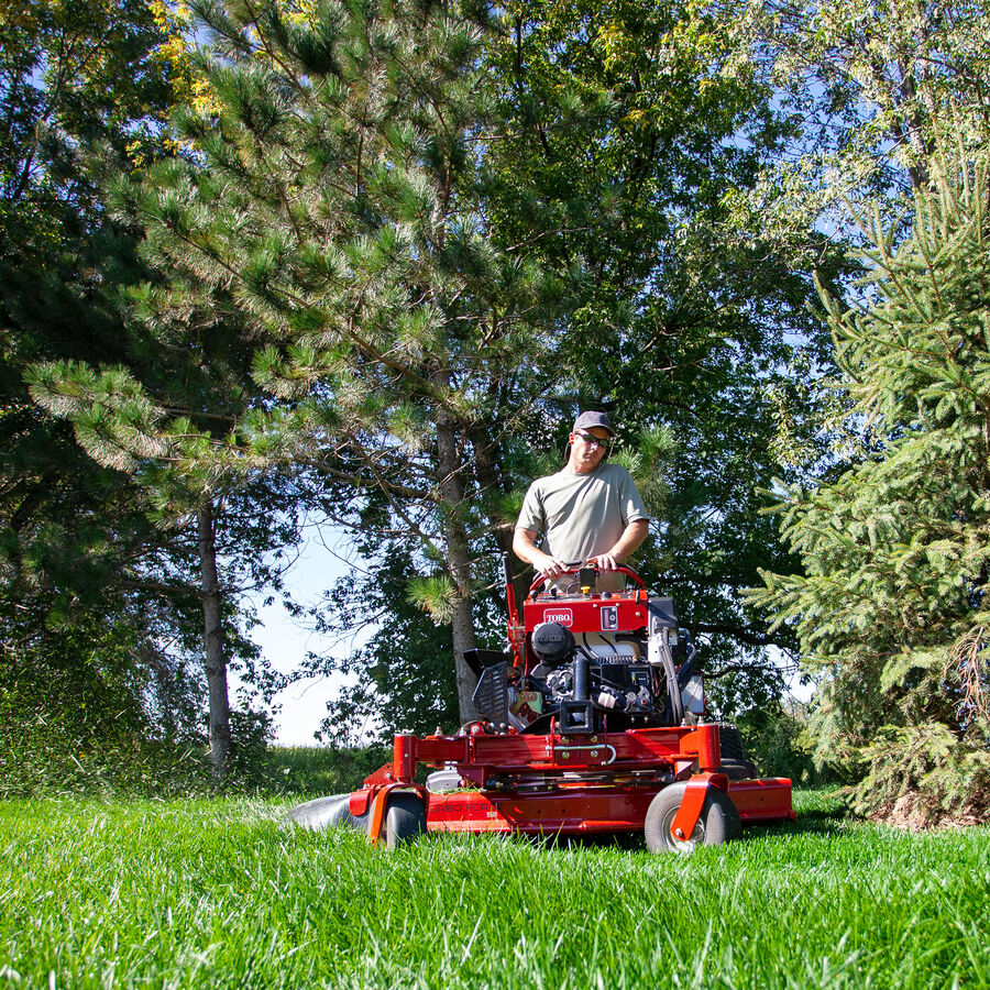 GrandStand® MULTI FORCE Stand-On Gas Mower in use - mowing in front of trees