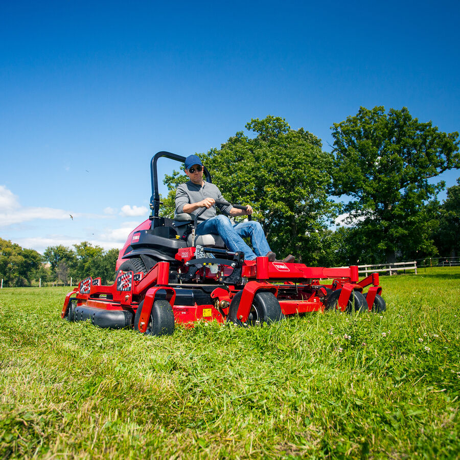 Man on a Toro Z Master 7500 series mower - mowing a large property with a fence and trees in the background.