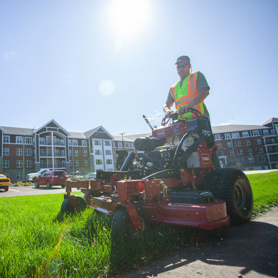 GrandStand® MULTI FORCE Stand-On Gas Mower in use - mowing the lawn of an apartment complex