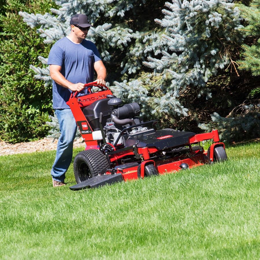 Man mowing with a Toro Proline Midsize mower mowing up a slight incline with pine trees to his left of the mower.